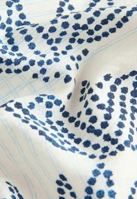 Witte stof met blauwe gestippelde cirkelpatronen en lichtblauwe rasterlijnen, met zachte plooien en textuurdetails.