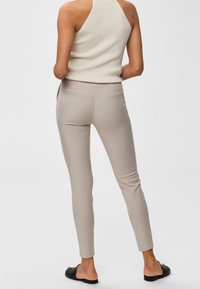 Beige skräddarsydda byxor med en slät yta, med bakfickor. Bärs med en ärmlös ljus topp och svarta slip-on sandals.