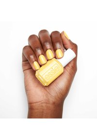 Vernis à ongles jaune brillant dans un flacon en verre transparent avec un capuchon blanc, tenu dans une main marron avec des ongles bien entretenus peints en jaune.