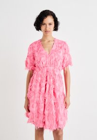 Ροζ φόρεμα με V-λαιμόκοψη, κοντά μανίκια και στρωτή υφή με φούντες σε όλη την επιφάνεια. Η μέση είναι συρραμμένη για καθορισμένη σιλουέτα.