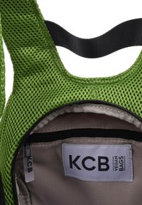 Bolsa de malla verde con una correa negra, que cuenta con un bolsillo interior con cremallera y una etiqueta que dice "KCB VEGAN BAGS."