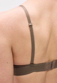 Κοντινή λήψη του άνω μέρους της πλάτης ενός ατόμου που φοράει καφέ ρυθμιζόμενο λουρί σουτιέν με κούμπωμα άγκιστρο και ματιού.