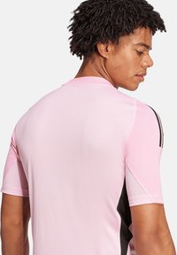 T-shirt de sport à manches courtes en rose clair avec des accents noirs et des panneaux en mesh, présentant un col rond et une coupe ajustée.