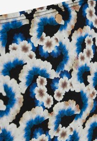 Tessuto floreale con motivi di fiori in tie-dye blu, bianco e beige, e un piccolo bottone rotondo in metallo dorato.
