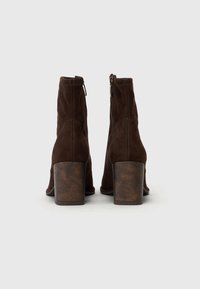 Bottes à chevilles en daim marron avec un talon bloc texturé et à motif. Elles possèdent une fermeture éclair, des détails cousus et une silhouette élégante.