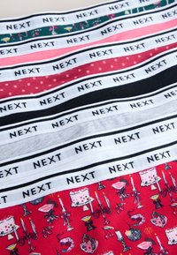 Rangées de tissus de différentes couleurs et motifs, chacune avec une bande d'étiquette blanche imprimée à plusieurs reprises avec le mot « NEXT » en texte noir.