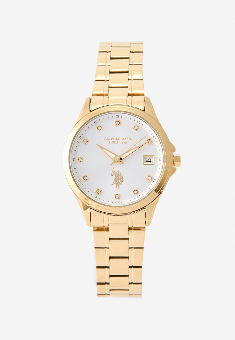 Reloj de pulsera en tono dorado con un dial blanco, marcadores dorados y un logo. Cuenta con una correa de eslabones y una pantalla de fecha en la posición de las 3 en punto.