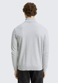 Siva pletivna turtleneck džemper sa dugim rukavima. Mekana tekstura i ravni kroj, s bočnom oznakom i minimalističkim dizajnom.