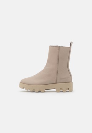 Beiger Leder-Stiefel mit Zuglasche, seitlichem Reißverschluss, klobiger Sohle und Marc O'Polo-Logo, das in der Fersenpartie geprägt ist.