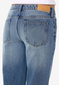 Τζιν παντελόνι σε ανοιχτό μπλε χρώμα με φθαρμένο φινίρισμα. Διαθέτει δύο πίσω τσέπες και μια καφέ δερμάτινη ετικέτα με το λογότυπο "NOISY MAY" στη ζώνη.