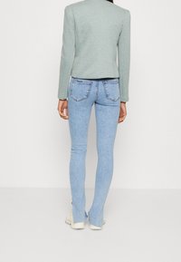 Un jean skinny bleu clair présente un design classique à cinq poches avec des poches arrière, associé à un blazer vert menthe texturé et ajusté.