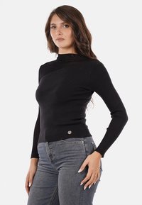 Maglione nero a coste con collo alto e maniche lunghe, caratterizzato da una silhouette aderente e un piccolo patch con logo sul davanti.