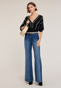 Czarny kardigan w turkusowe paski, w połączeniu z dzwonowymi niebieskimi dżinsami. Dodatki to beżowa torebka i kremowy pasek. Widoczne gładkie tekstury.