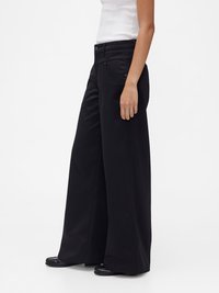 Pantalon noir à jambes larges en tissu doux, avec une ceinture à taille mi-haute, des poches devant et derrière, et une texture lisse.