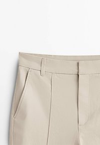 Pantalons beiges avec une texture lisse, dotés d'une taille plate, d'un devant à double plis et de poches latérales.