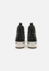Zapatillas altas de tela negra con acentos con tachuelas, que presentan formas de corazón y cuadrado, franjas blancas en contraste y una suela gruesa.
