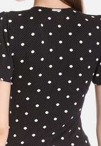 Svart tyg med små vita prickar; har korta ärmar och en samlad halsringning; slät textur med en lätt känsla.