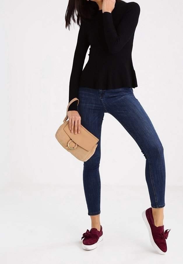 Haut noir à manches longues côtelé, ourlet peplum, associé à un jean skinny bleu foncé. Sac à main beige avec un accent circulaire, baskets bordeaux avec un nœud.