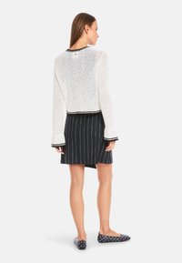 White mesh long-sleeve sweater with black trim, paired with a navy pinstriped skirt and polka dot flats. Back view shows texture and design details.
