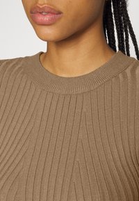 Maglione lavorato a coste marrone con scollatura rotonda. La trama presenta righe verticali e una sensazione morbida e elasticizzata.
