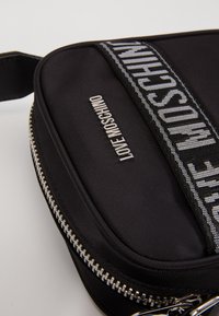 Černá obdélníková crossbody taška se stříbrným zipem, kovovým logem "LOVE MOSCHINO" a odpovídajícím textilním popruhem s potiskem loga.