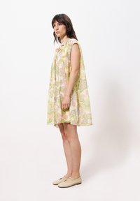Ärmelloses Kleid mit floralem Muster in Pastellfarben, das ein fließendes Design aufweist. Knielang mit subtiler Schicht und leichtem Stoff.