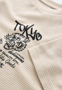 Felpa beige con motivo a motivo trapuntato, caratterizzata da una grafica di tigre nera e scritta "TOKYO". Girocollo a costine e design a vestibilità casual.