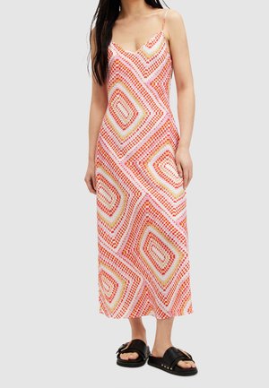 Femme portant une robe sans manches, longue jusqu'aux chevilles, avec un motif géométrique de points orange, rose et jaune et des sandales slides noires.