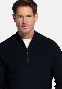 Marineblauwe trui met ritssluiting in de hals, met ribbelstructuur en gestructureerde kraag. Voorzien van een halve rits en contrasterend detail aan de binnenkant van de kraag.