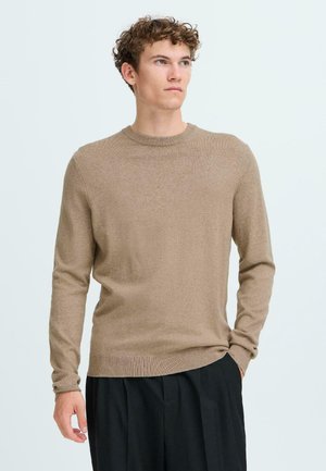 Brun strikket genser med lange ermer og rund hals. Myk tekstur og slim fit, kombinert med svarte bukser.