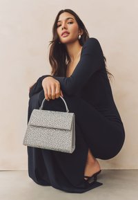 Bolso gris con un diseño estructurado, adornado con cristales brillantes de varios tamaños. Cuenta con una solapa segura y un asa superior.