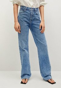Jeans de tiro alto en azul claro con una silueta de pierna recta. Hechos de mezclilla con costuras visibles y diseño de cinco bolsillos.