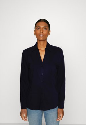 Navy button-up shirt with long sleeves, collar, and a smooth texture, paired with light blue jeans. Simple, solid color design.