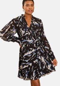 Juoda suknelė su plevėtota medžiaga, turinti mėlynus ir pilkus abstrakčius raštus, ilgos rankovės ir suderinta diržo detalė. V formos iškirpė ir tekstūruota detalė.