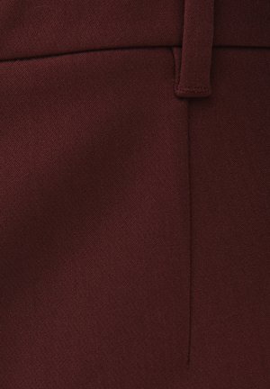 Primo piano di un tessuto bordeaux con una cucitura verticale e un passante per cintura cucito sul bordo superiore.