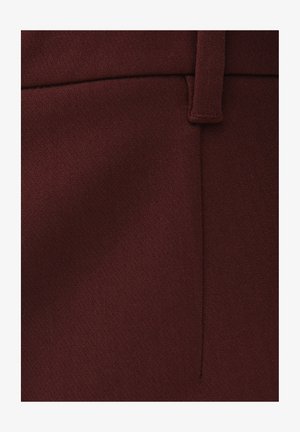 Primo piano di un tessuto bordeaux con una cucitura verticale e un passante per cintura cucito sul bordo superiore.
