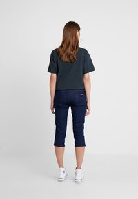 Mörkgrå topp med korta ärmar kombinerad med mörka denimcapripants och vita sneakers. Mjukt tyg med avslappnad passform och midjehöjd.