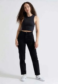 Jeans pretos de cintura alta com pernas ajustadas, combinados com um top cropped canelado cinza escuro. A modelo usa ténis brancos, apresentando um look casual.