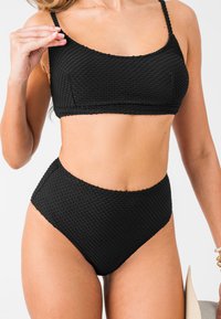 Conjunto de bikini negro con tejido texturizado y patrón en cuadrícula, que incluye un top corto y una parte inferior de talle alto, ambos con tirantes finos.