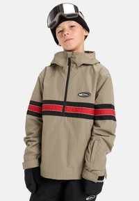 Beige waterdichte jas met rood en zwarte horizontale strepen. Beschikt over een kwart rits, verstelbare manchetten en een logo patch op de borst.