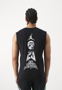 Černé tílko bez rukávů s potiskem na zádech, který zobrazuje lebku, číslo "23" a logo Jumpman v bílé barvě. Měkký bavlněný materiál a volný střih.
