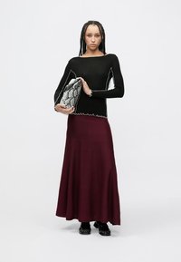 Czarna bluzka z długim rękawem z białymi przeszyciami, zestawiona z bordową maxi spódnicą. Całość dopełnia torebka w wzór wężowy oraz czarne buty.