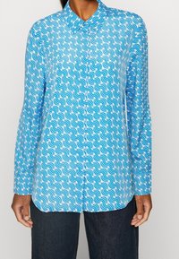 Camicia blu a maniche lunghe con motivo ondulato in diverse tonalità di blu e bianco; chiusura con bottoni e colletto classico.