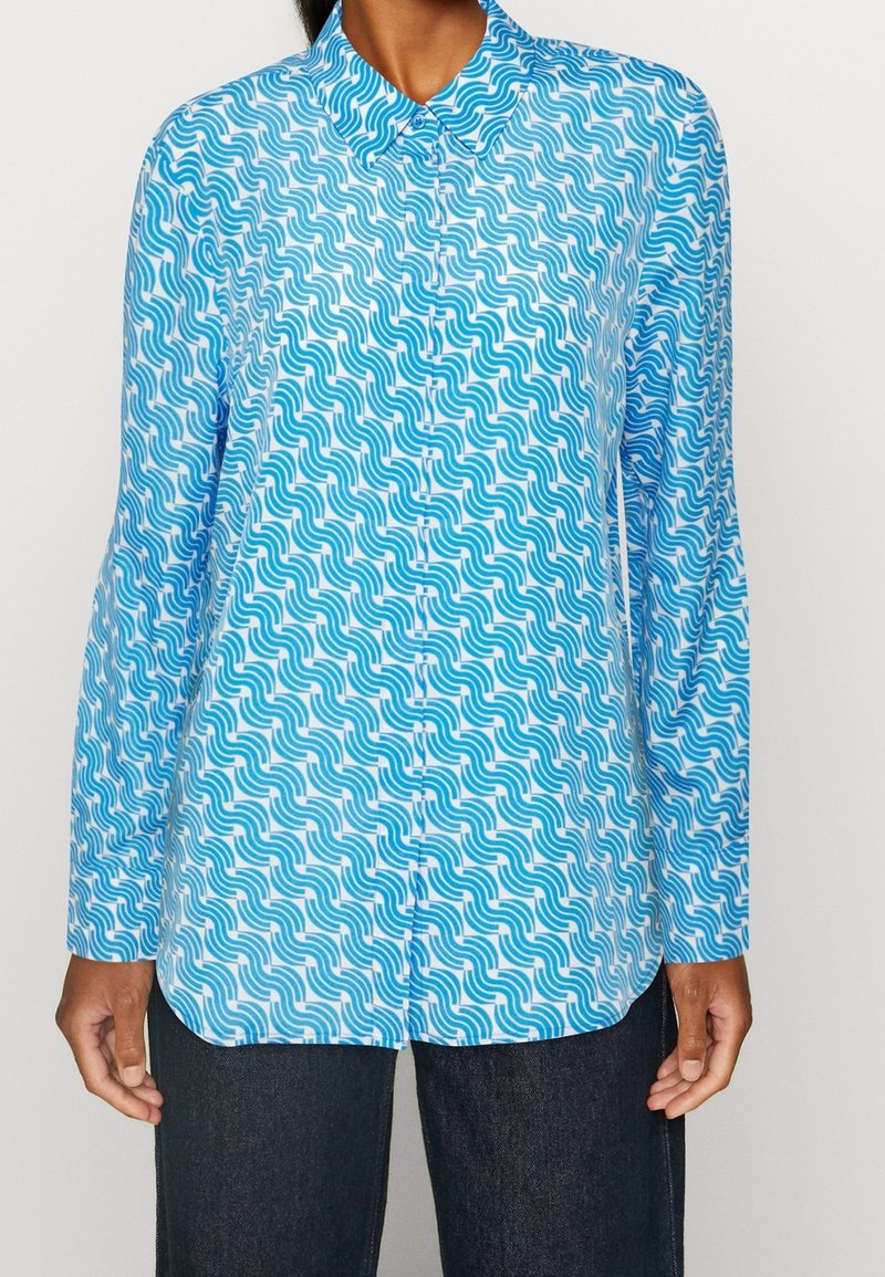 Camicia blu a maniche lunghe con motivo ondulato in diverse tonalità di blu e bianco; chiusura con bottoni e colletto classico.
