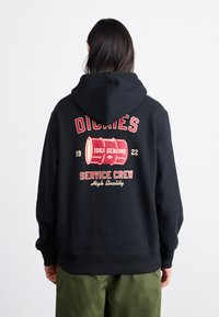 Felpa nera con grafica rossa che presenta un barile, testo "DICKIES", "100% GENUINO" e "SERVICE CREW" in stile vintage.