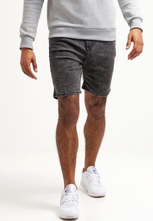 Shorts en denim noir avec un délavage usé, présentant un design classique à cinq poches et un ourlet effiloché. Associés à des baskets blanches.