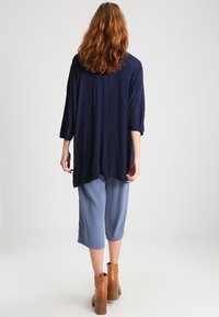 Granatowa oversize bluzka z rękawami do łokcia, połączona z jasnoniebieskimi kulotami i brązowymi botkami na słupku. Gładka tekstura tkaniny.