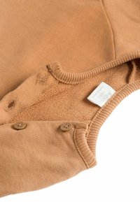 Vihreä puuvillapuku pyöreällä pääntieellä, jossa on kaksi napitusklipsiä ja kudottu etiketti. Teksturoitu kangas kauluksessa ja hihansuissa.