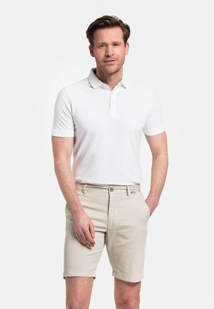 Polo shirt blanc à manches courtes avec col et trois boutons, associé à un short beige clair avec une fermeture à un seul bouton.