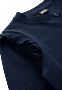 Close-up of navy blue knit garment sleeve featuring ruffled edge detail and a button near the collar area.